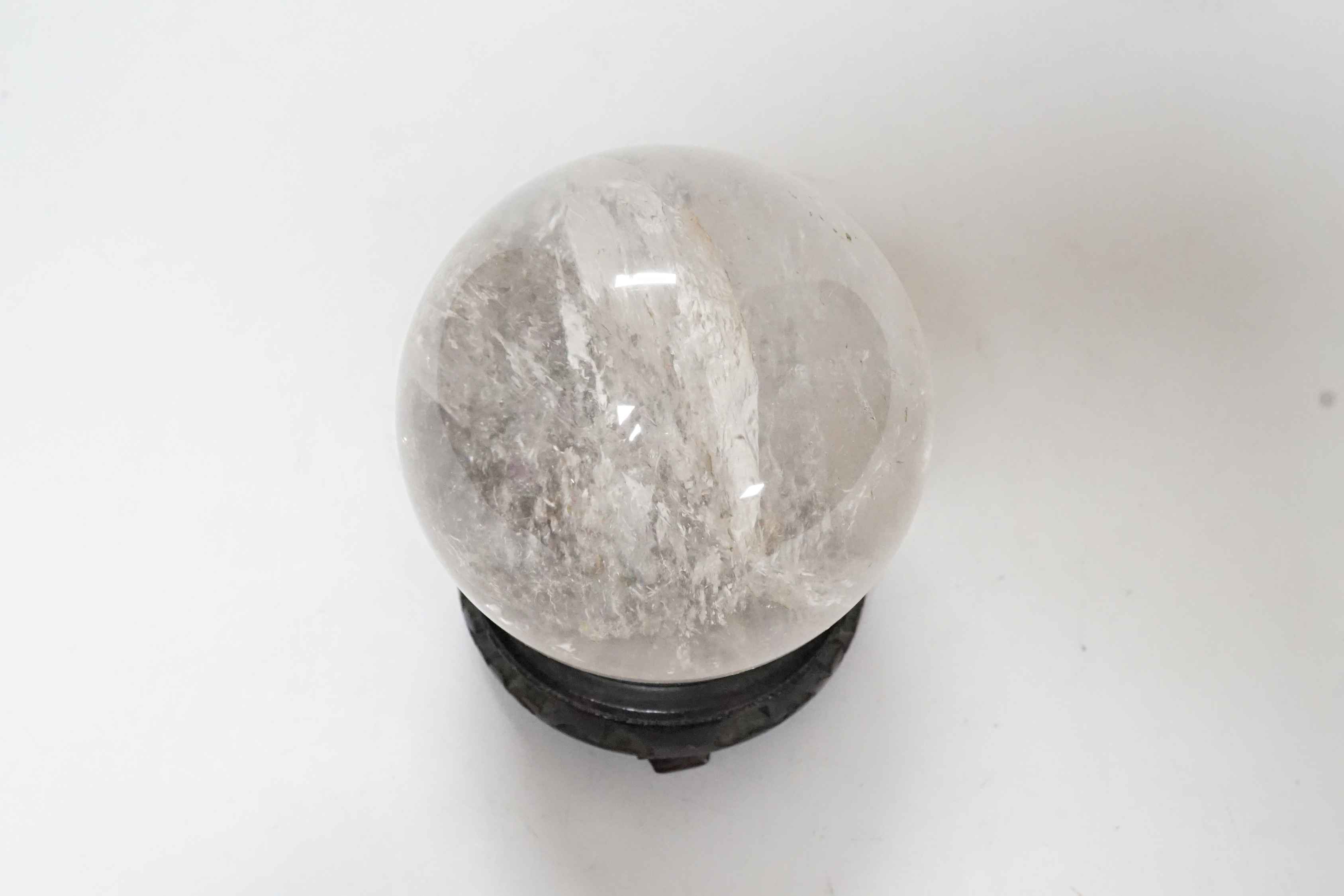 A rock crystal quartz sphere, probably from Brazil, on a carved wood stand, 10cm tall